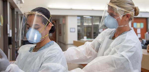 Medical personnel don PPE before entering a COVID-19-positive, non-critical patient’s room.