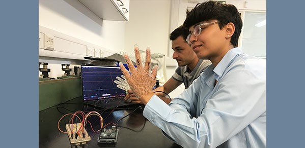 Sara AlMahri is pictured providing a demo of the 'smart glove'. Behind her is Ivan Grega, monitoring the glove's interactions on a laptop in real time.