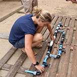 Francesca is on the floor assembling the chlorine test rig while in Uganda. Someone stands over her, ready to assist.