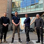 Four members of the Department’s Design and Technical Services team stand in a line on a partial zebra crossing on the grounds o