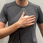 Human demonstrating use of a handheld device for heart disease screening. They are seen holding the device against their chest.
